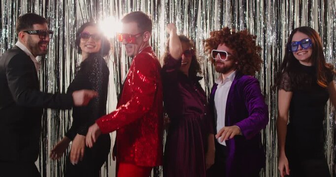 Funny happy people group in bright suits dancing together celebrating success at corporate party indoors. Young friends having fun at disco party clubbing in night club. 4k video. Slow motion.