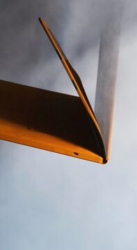 Terracotta orange laptop computer partially closed at an angle for a hardware review editorial shot against a light silver grey background with copy space
