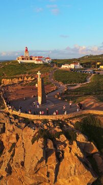 Cabo da Roca, Cape Roca, Cliffs and Atlantic Ocean at Sunset. Lighthouse and Cross. Portugal. Aerial View. Orbiting. Vertical Video