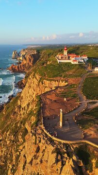 Cabo da Roca Lighthouse and Cross. Cape Roca, Cliffs and Atlantic Ocean at Sunset. Portugal. Aerial View. Drone Moves Forward. Distant Shot. Vertical Video