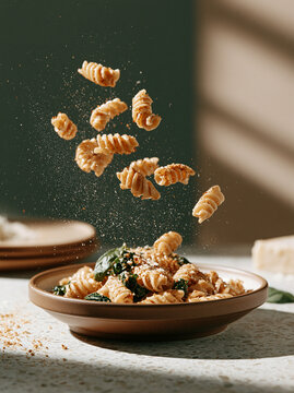 Levitating fusilli pasta with spices falling into a bowl with spinach and cheese