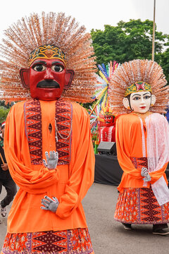 edium shot showcasing two Ondel-ondel puppets dressed in bright orange outfits.