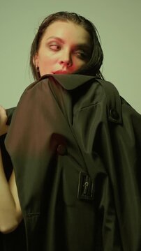 Medium shot portrait of young blue-eyed woman hiding face behind long black leather coat