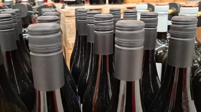 Multiple wine bottles with black screw caps on store shelf. Rows of dark glass bottles in retail display. Concept of wine production, alcohol variety, and modern packaging in beverage industry