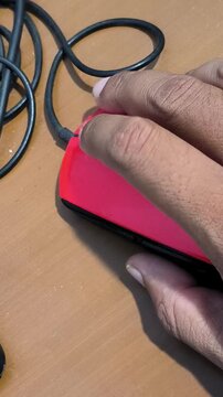 A person's hands holding a gaming mouse with long black cable on a wooden table.