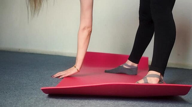 Horizontal video of fit woman in black sportswear performing standing forward fold with one hand on mat at home, gym, close up of athlete practicing balance and hamstring stretch for body wellness