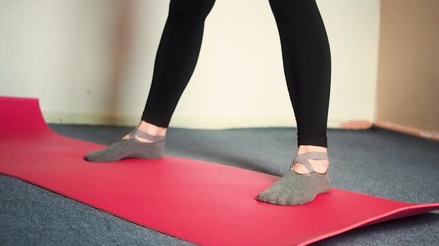 Horizontal video of a fit woman in black leggings picking up blue dumbbell on red mat at home or gym, close up of athlete hands and legs starting strength training workout for fitness and wellness