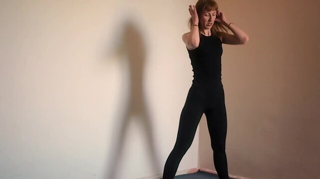 Horizontal video of fit woman in black sportswear doing forward fold and spine mobility exercises at home or gym, athletic girl practicing dynamic stretching and back flexibility for healthy lifestyle