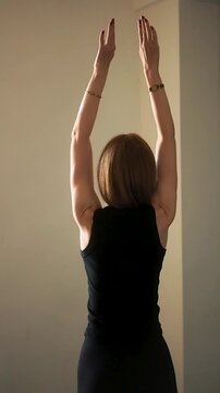 Vertical video of fit woman in black top doing back stretching and shoulder mobility exercises at home rear view of female athlete practicing arm swings and posture correction for wellness