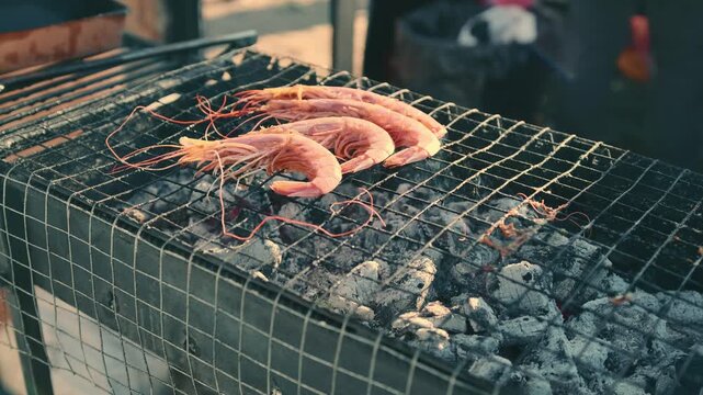 Fresh king prawn grilling over hot charcoal on outdoor metal grill. Seafood meal preparation in street food stall. Gastronomy cooking process for gourmet dinner.