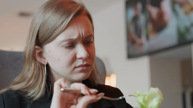 Woman skeptically probes lettuce with fork, close inspection of texture and dressing, furrowed brow and focused frown, tasting evaluation like food critic, studio cafe interior, focused lighting,