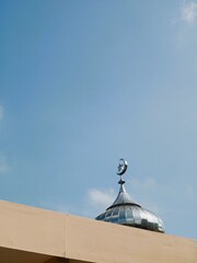 Naklejka premium A silver dome with a crescent moon finial atop a building against a clear blue sky, symbolizing Islamic architecture and faith.