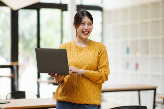Smiling young asian woman holding laptop working remotely