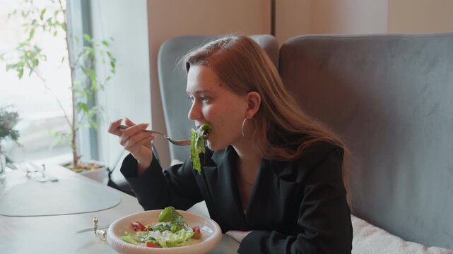 Professional woman enjoying meal. Caucasian lady dressed professionally testing healthy salad at restaurant. Elegant woman in business clothing sampling colorful salad at sunlit bistro table