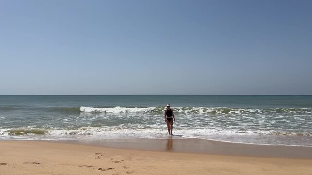 Young woman raising hands on beach. Summer holidays at tropical island. Small waves crashing on shore. Relaxation concept 
