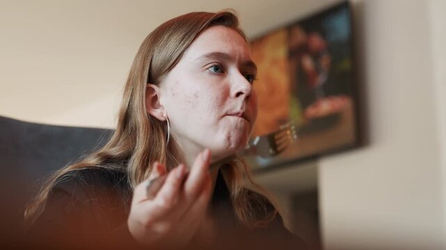 Young woman tasting leafy salad indoors, closeup of hesitant expression, fork with greens, living room background, warm soft lighting, casual sweater, subtle disappointment, candid everyday moment