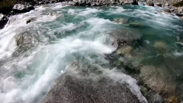 Fast flowing turquoise water rushing over rocks and creating white water rapids in a pristine mountain river.
