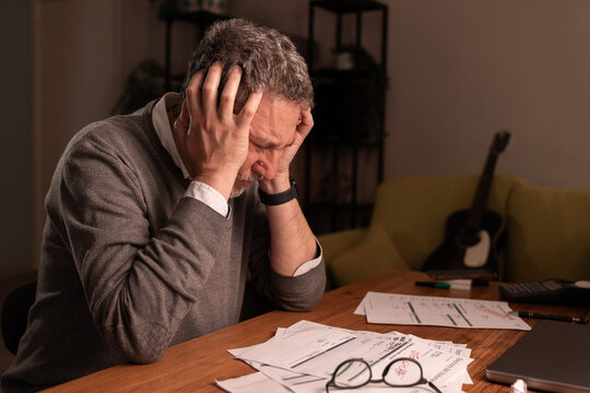 Senior man overwhelmed by financial stress at home with unpaid bills and mental breakdown