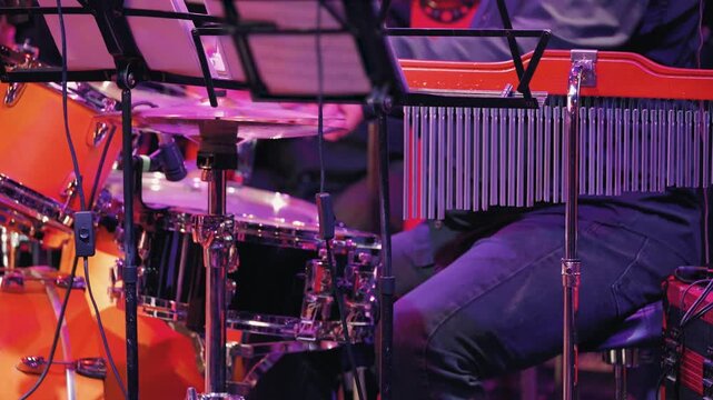 A close-up of a drum kit and percussion instruments on stage. The drummer plays with drum brushes. The atmosphere is reminiscent of a live musical performance or jazz concert