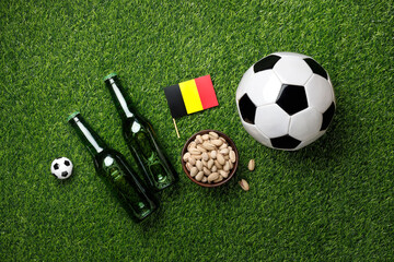 Naklejka premium Soccer balls, two green beer bottles, bowl of pistachios and Belgian flag on green grass create the perfect match day viewing atmosphere. Top view, flat lay.