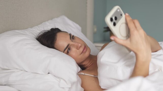 Young woman in bed with smartphone, transitioning from sleep to digital engagement. Concept technology lifestyle and morning routine.

