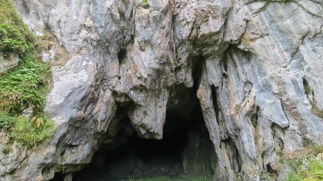 An upward camera sweep reveals the towering entrance of Cuevallagar Cave, highlighting its dramatic limestone walls within the protected mountains of Yernes y Tameza, Asturias.