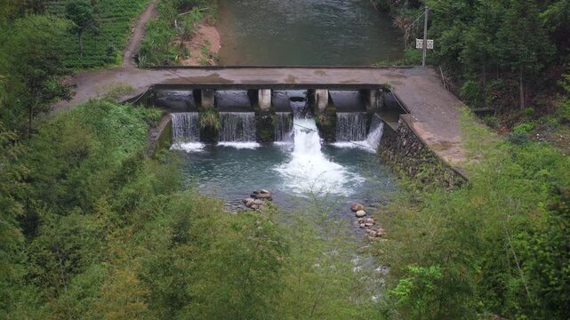 Mountain stream flowing over a concrete weir dam with cascading water and lush green surroundings