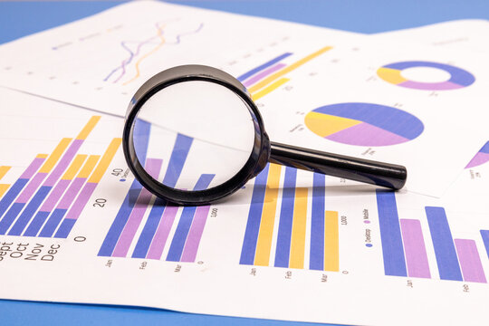 Close-up of a magnifying glass enlarging quarterly data on colorful business charts and graphs.