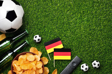  A soccer balls, green beer bottles, potato chips, German flags and TV remote on green grass create the perfect game viewing atmosphere for fans. Top view with copy space. © PixelArt_25