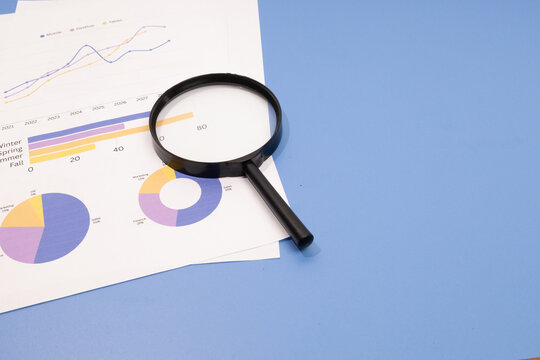 Magnifying glass on financial charts and data reports over a blue background for business analysis concept.