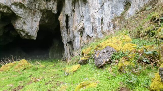 A horizontal camera sweep reveals the wide rocky entrance of Cuevallagar Cave, emphasizing the textured limestone walls and the natural scale of this protected mountain landscape in Asturias