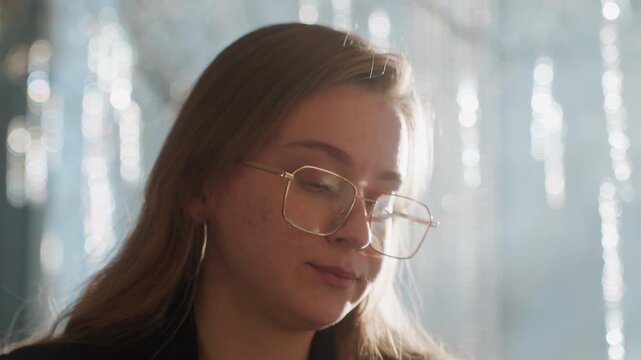 Closeup white freelancer raising cup, backlit sparkle window with shimmering bokeh, gold frames and hoop earrings, thoughtful pause during writing session, relaxed urban vibe and soft daylight