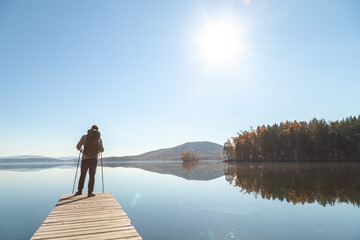 Naklejka premium A man admires the landscape of a mountain lake while standing on the pier
