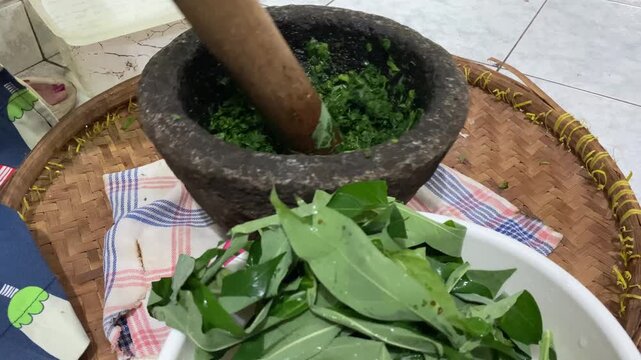 Hands are pounding pounding cassava leaves and pumpkin pieces use mortar and pestle made of stone. 