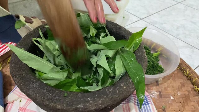 Hands are pounding pounding cassava leaves and pumpkin pieces use mortar and pestle made of stone. 
