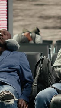 Vertical video Sleeping on chairs, departure board screen and tourists tired in airport after flights got cancelled. Napping, bench and exhausted travelers waiting for delayed flight updates, camera A