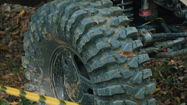 Close up view of dirty, rugged all terrain vehicle tire waiting behind yellow black barrier tape