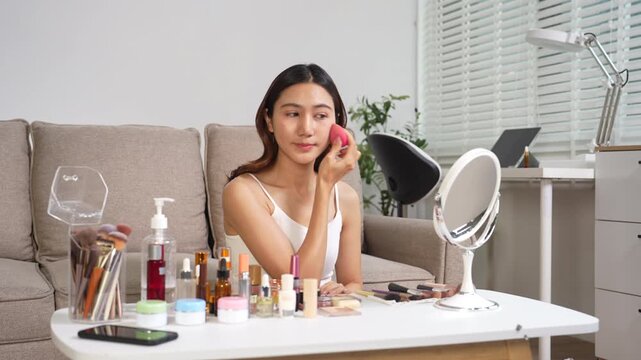 Asian beauty influencer recording makeup tutorial at home with smartphone, skincare and cosmetics content creator livestream.