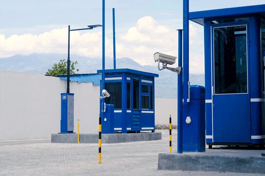Blue security booth stands firm against clear sky. Surveillance camera watches over access point vigilantly. 