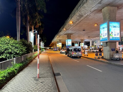 Night view of the ground level arrival and departure curb at Tan Son Nhat International Airport (SGN), Ho Chi Minh City, featuring terminal lighting and large billboards, 2025 