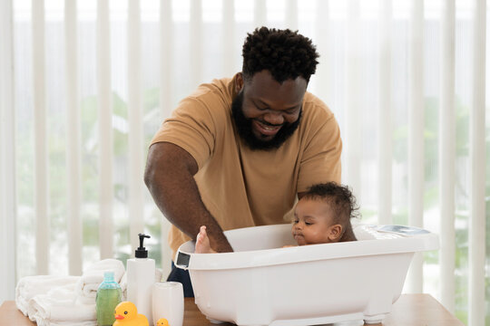 Cute baby taking bath in tub of water at home. African American newborn baby taking bath in bathtub with father. Little newborn child enjoying in bath time