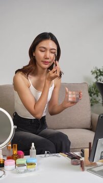 Asian beauty influencer recording makeup tutorial at home with smartphone, skincare and cosmetics content creator livestream.