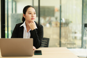 Fototapeta premium Thoughtful Asian businesswoman contemplating new ideas for her freelance business, looking into the future while developing creative solutions from her modern office