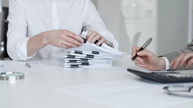 Professionals handling a large stack of documents and paperwork, signing a contract in a busy office. Audit and taxes in business