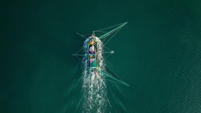 Cinematic bird's-eye view of an authentic wooden fishing boat navigating calm ocean waters in Southeast Asia.