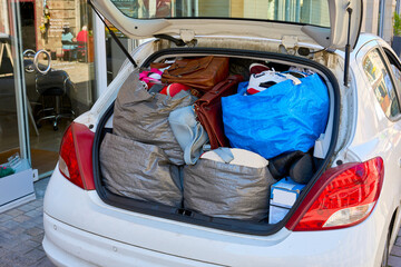 Open trunk of a white car stuffed with bags of clothes, shoes, and luggage. Concept of moving house, road trip, travel, or donation for charity. © beautiful-photo.de