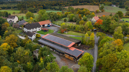 Aerial view showing solar panels on farm roofs surrounded by autumn trees in menden, germany © Karina