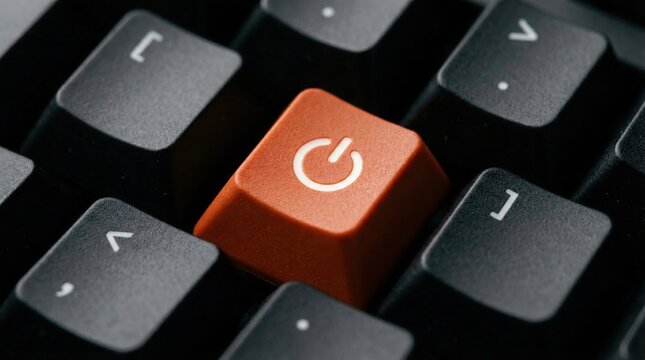 Bright orange power button key standing out on a dark computer keyboard representing technology control and system shutdown concepts in a modern office setting