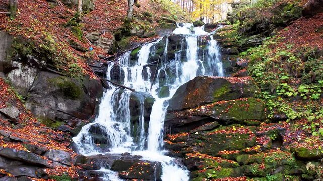 Narrow stream falling down mountain slope in autumn forest