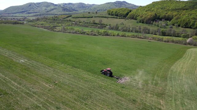 Aerial view of a red tractor plowing a vast green meadow. Beautiful rural scene with the agricultural machine cultivating the fertile soil
